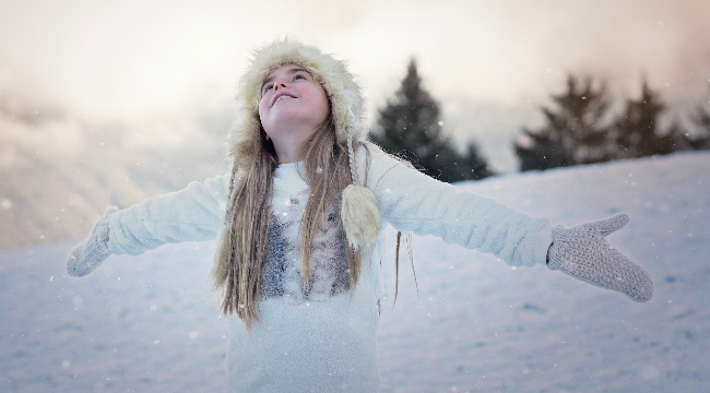 A young girl in winter clothing playing in the snow